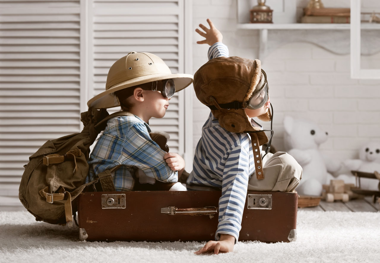 2 children in a suit case with exploring costumes on, pretending to be explorers on a boat