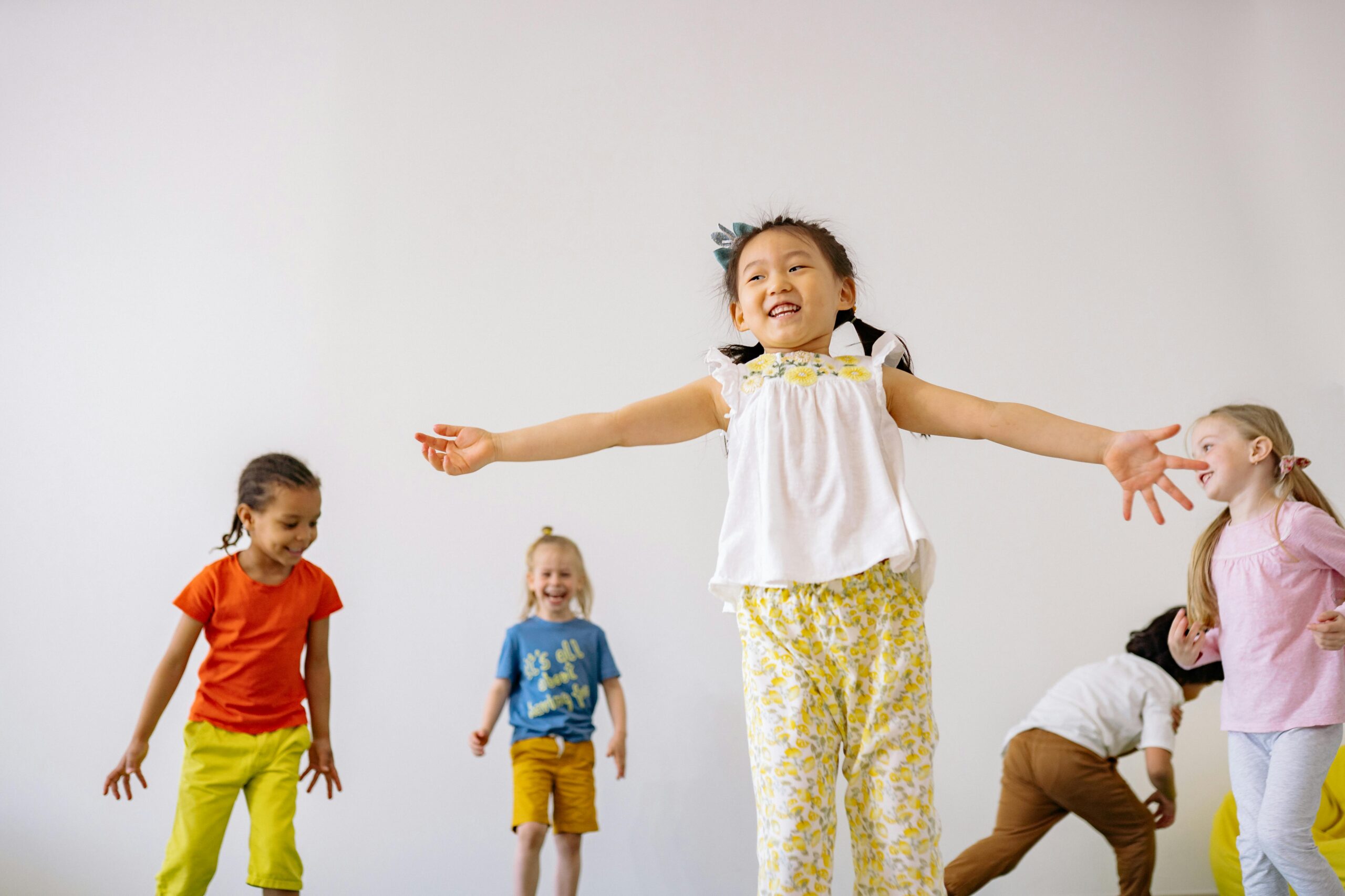 little girl moving around with her hands in the air while other children watch her in the background