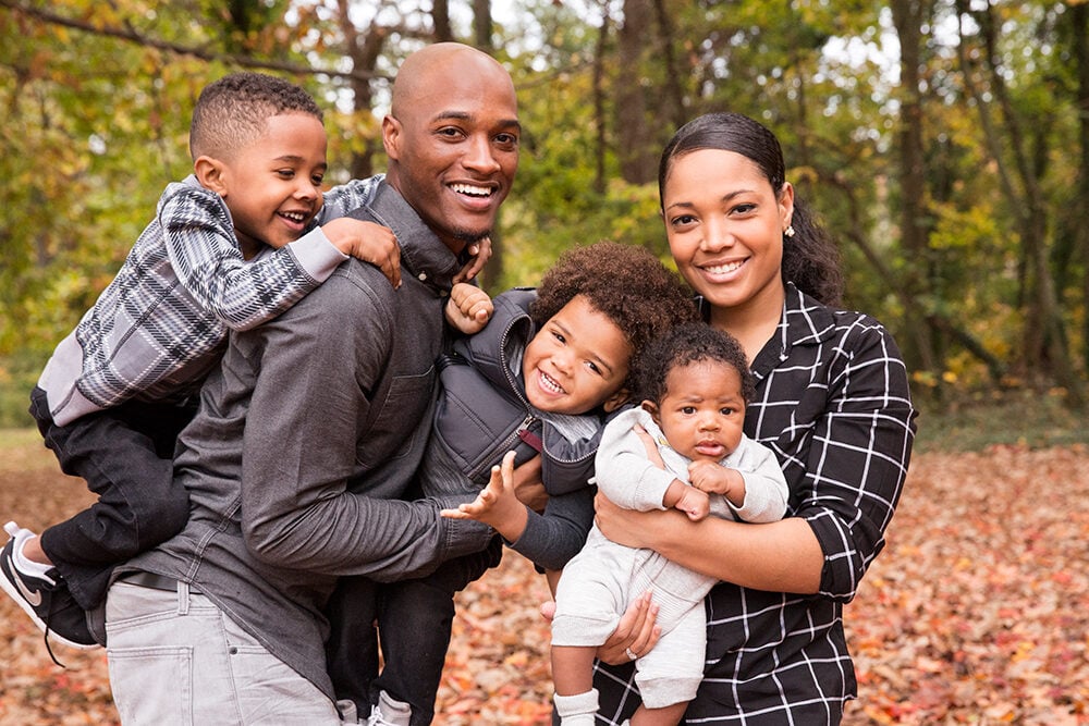 father and mother holding three children outside with trees in the background