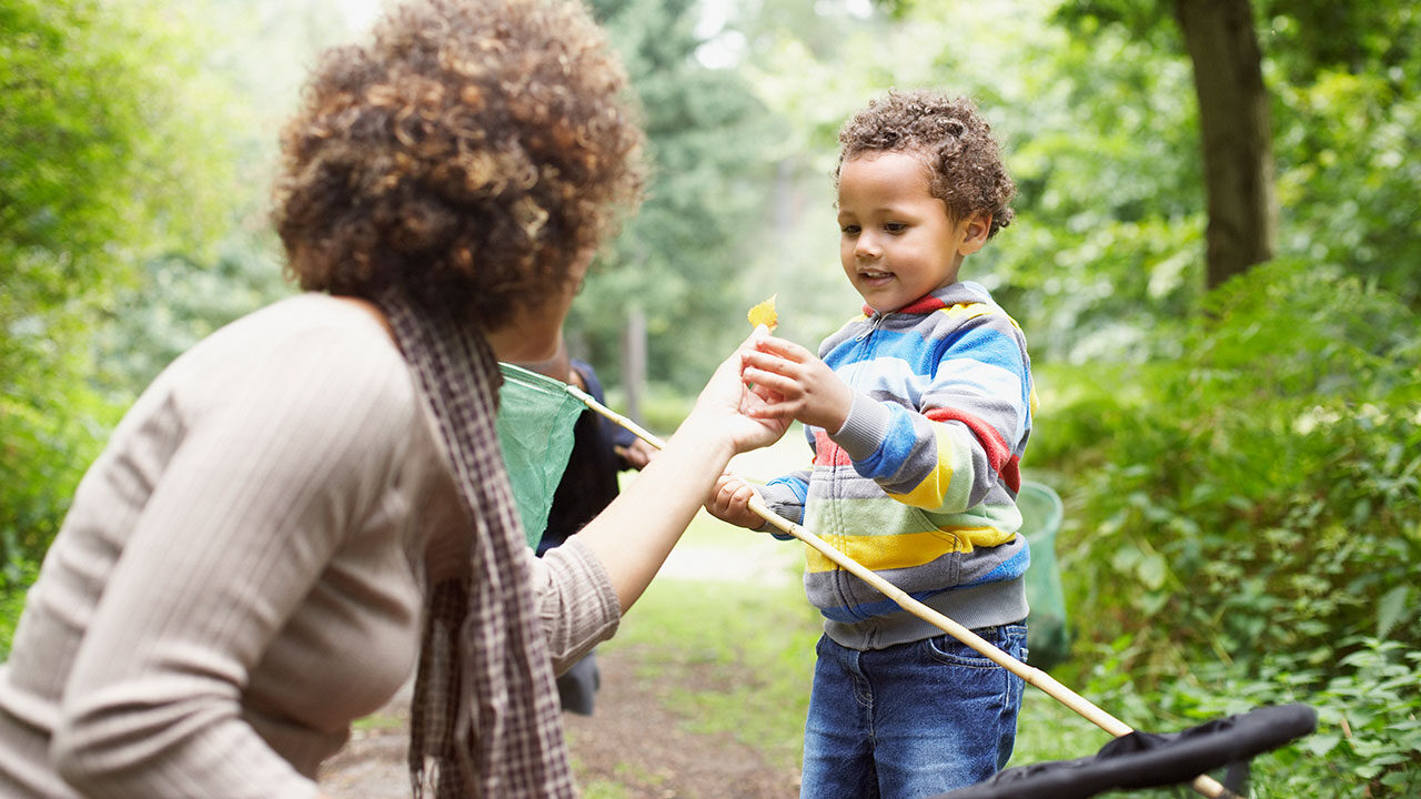 women giving a toy to a child while outside in the woods