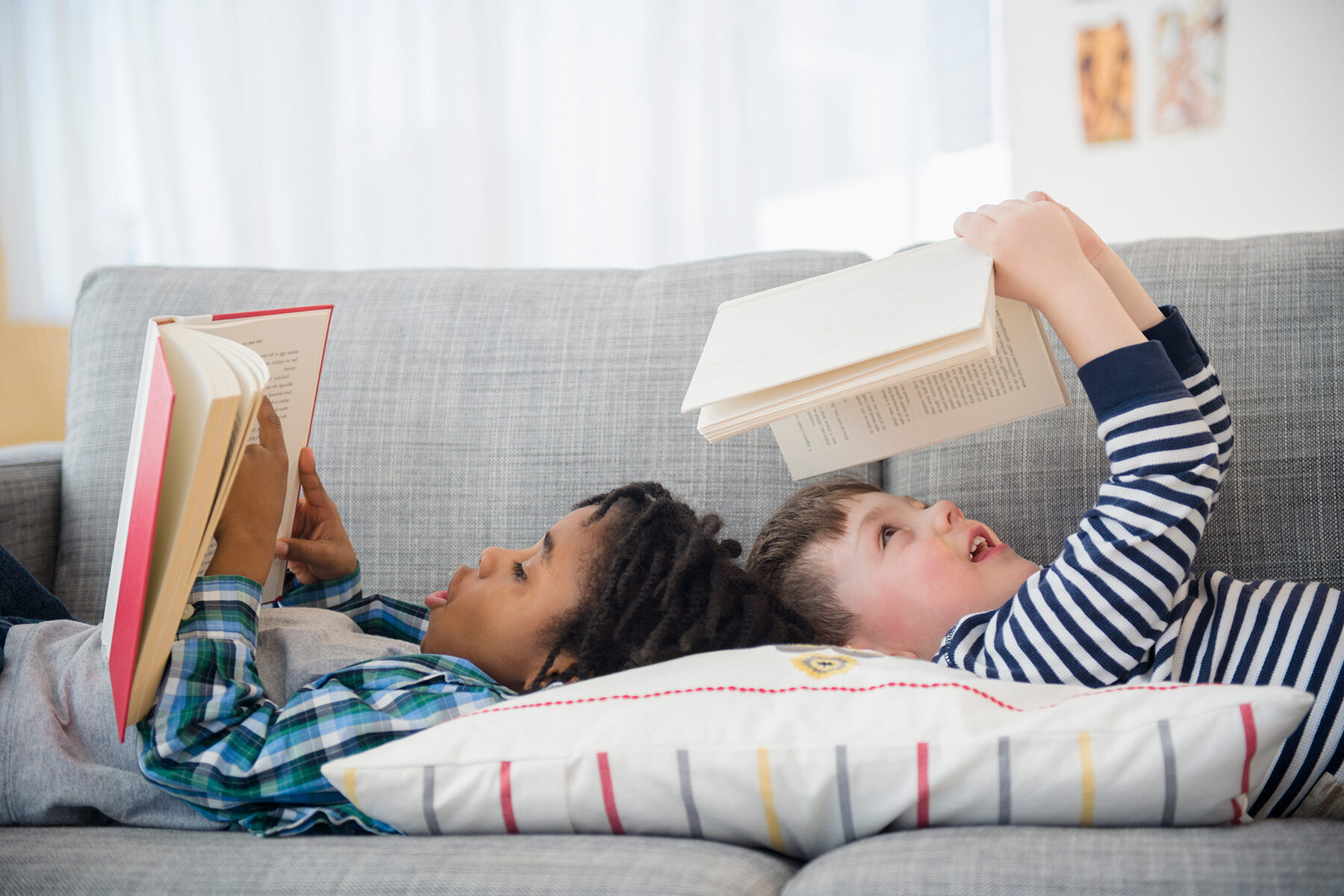 two kids laying on a couch reading books