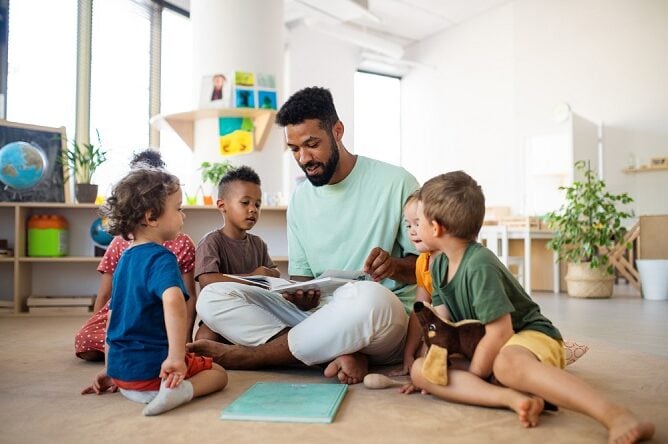 male sitting on the floor with children sitting around him reading a french for kids book